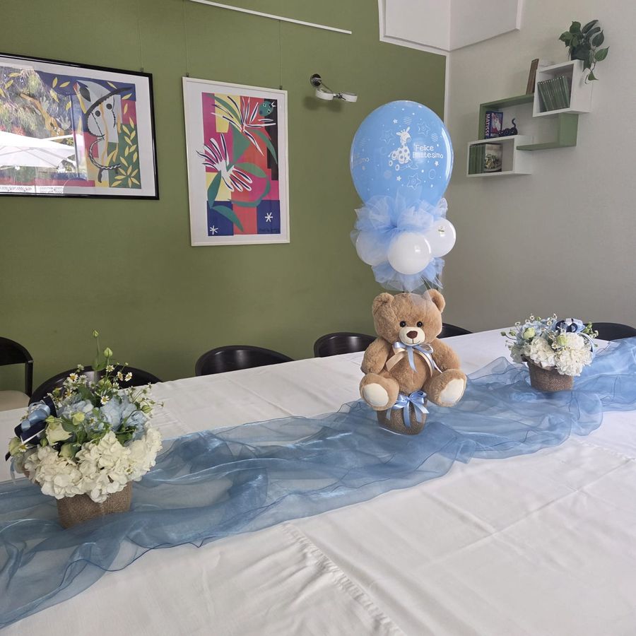 Tavolo per battesimo con palloncino 'Felice Battesimo', orsacchiotto e composizioni di ortensie bianche e azzurre in vasi di juta