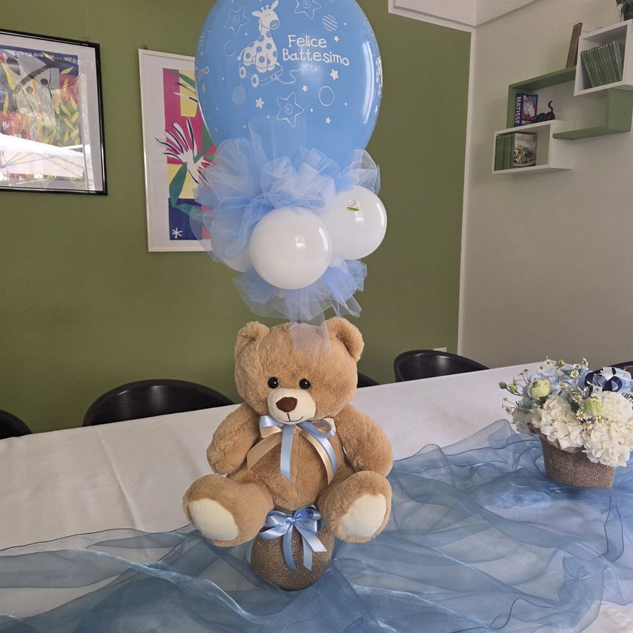 Allestimento da battesimo con orsetto di peluche, palloncino azzurro 'Felice Battesimo' e tulle celeste su tavolo