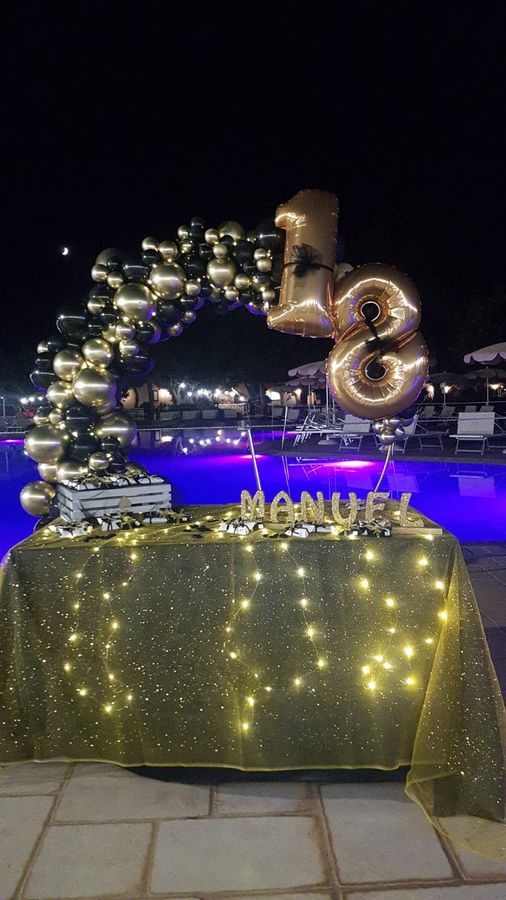 Allestimento per festa di diciottesimo compleanno a bordo piscina con arco di palloncini oro e neri, numeri 18 e tavolo della confettata luminoso