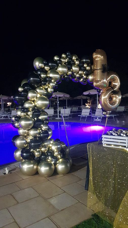 Arco organico di palloncini oro e neri a bordo piscina illuminata di notte, con numero 18 in mylar dorato
