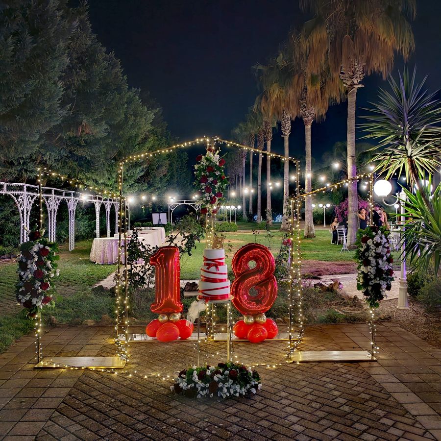Allestimento per festa di diciottesimo compleanno: struttura luminosa dorata con composizioni bordeaux e bianche, palloncini numero 18 e torta a piani