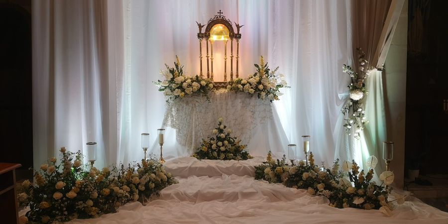 Allestimento floreale liturgico in chiesa: altare drappeggiato di bianco con rose avorio, anthurium e candele su alzate