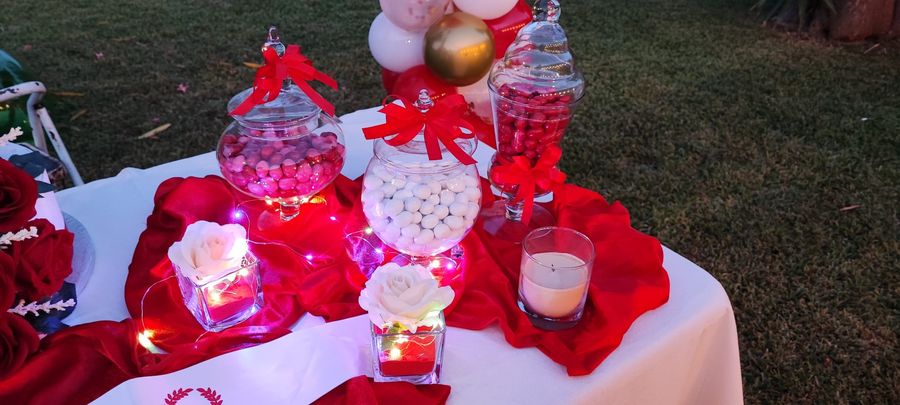 Confettata di laurea in giardino con vasi di confetti rossi e bianchi, fiocchi rossi, rose in cubi di vetro, candele e luci a filo