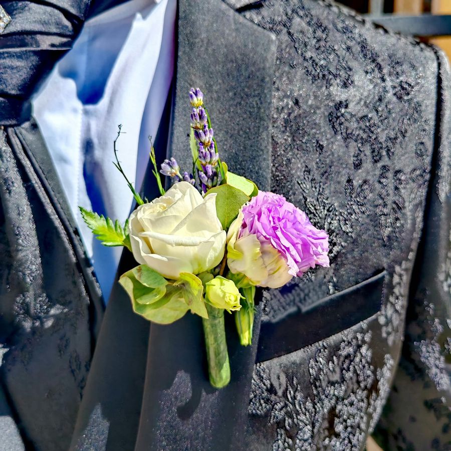 Bottoniera dello sposo con rosa bianca, lisianthus lilla, lavanda ed eucalipto sul revers della giacca damascata