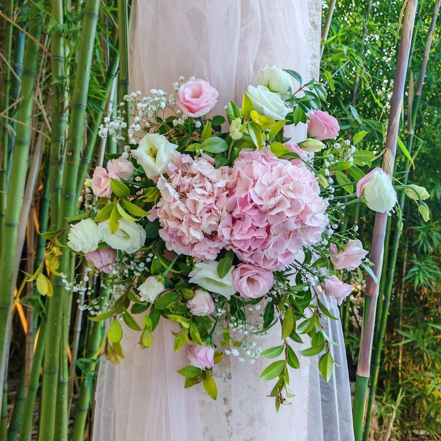 Composizione di ortensie rosa, lisianthus bianchi e rosa e gypsophila fissata su una colonna drappeggiata di tulle rosa cipria, tra i bambu'