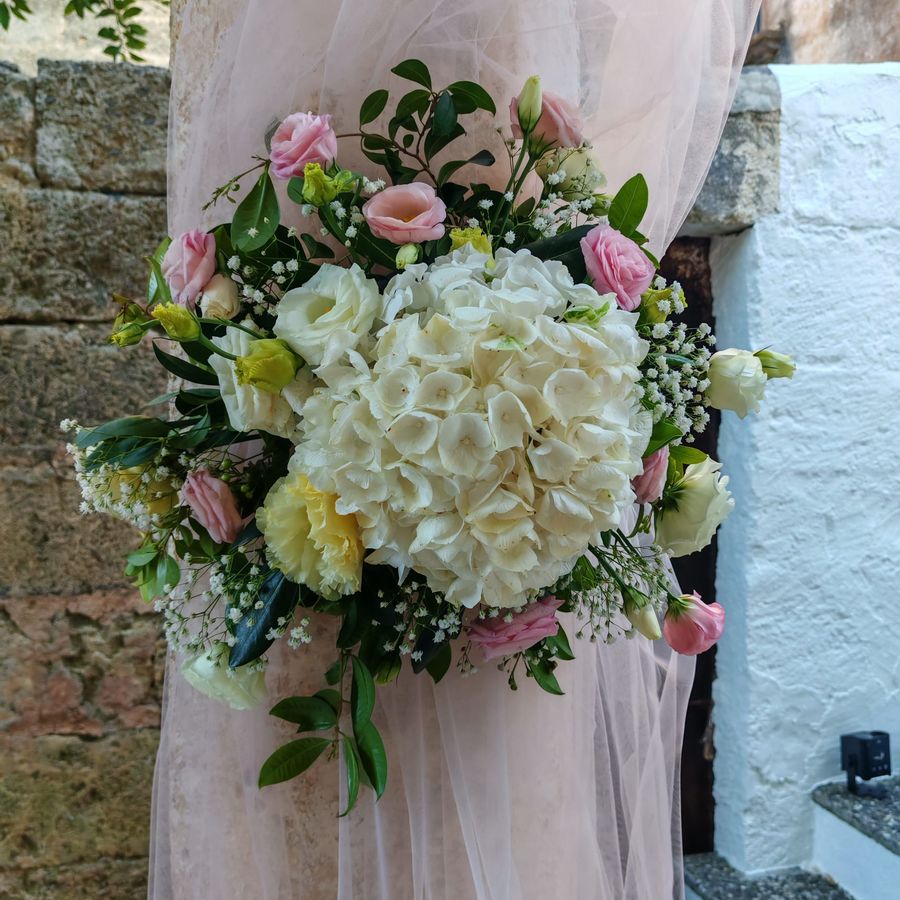 Composizione tonda di ortensia bianca, lisianthus rosa e gypsophila fissata su una colonna rivestita di tulle rosa cipria
