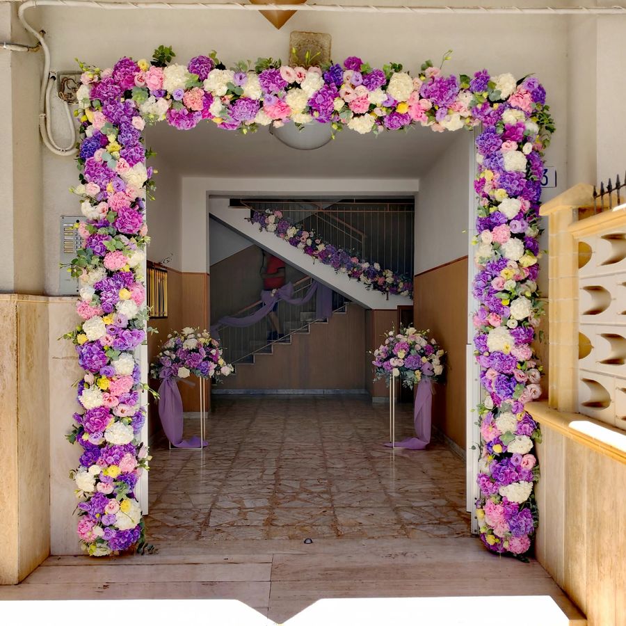 Arco floreale su portone d'ingresso con ortensie e rose lilla, rosa e bianche, colonne fiorite e drappi di tulle viola