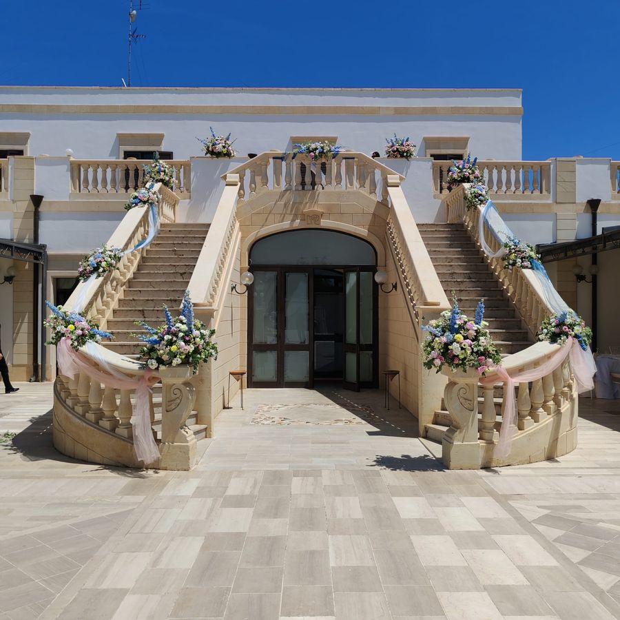 Scalinata monumentale di villa per ricevimenti addobbata con composizioni di delphinium azzurro, rose e lisianthus rosa e drappi di tulle