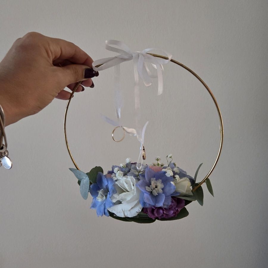 Portafedi circolare dorato con fiori azzurri e bianchi e fedi nuziali appese a nastri di raso