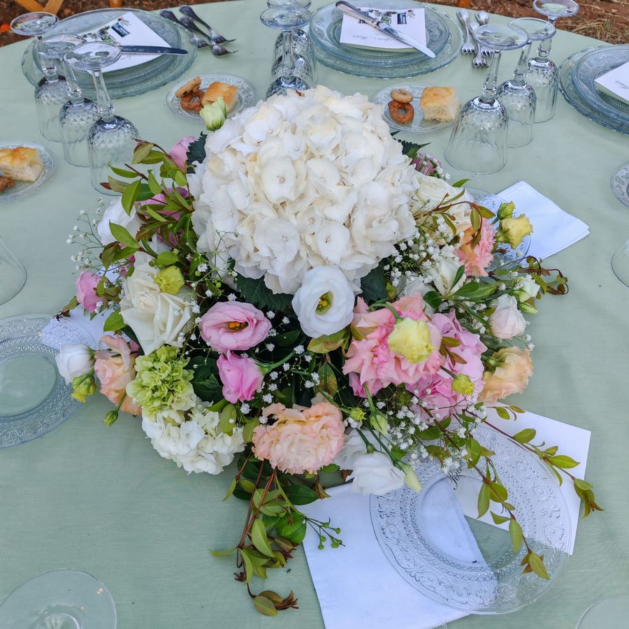 Centrotavola basso di ortensie bianche, lisianthus rosa e rose su tavolo di ricevimento all'aperto con tovaglia verde salvia