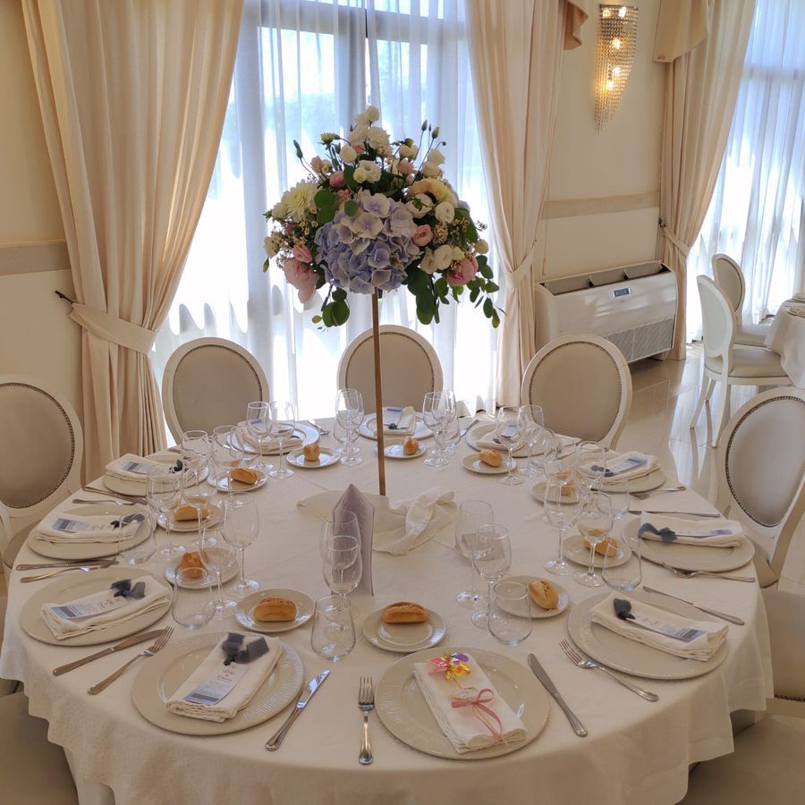 Tavolo rotondo del ricevimento con centrotavola alto di ortensie azzurre, rose e lisianthus in sala elegante